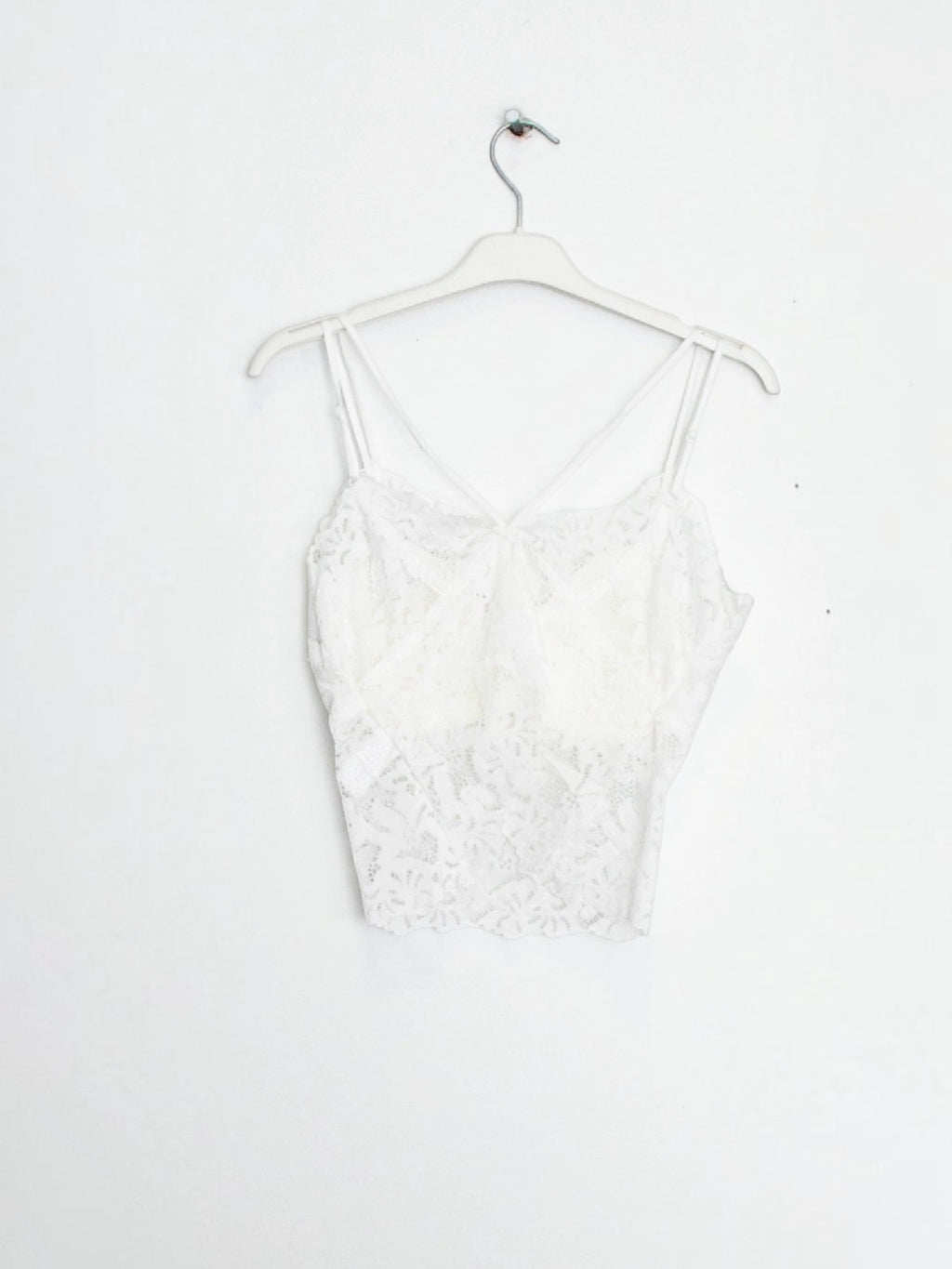 BROCK white lace crop top tank with built-in cups and delicate spaghetti straps hanging on a white hanger