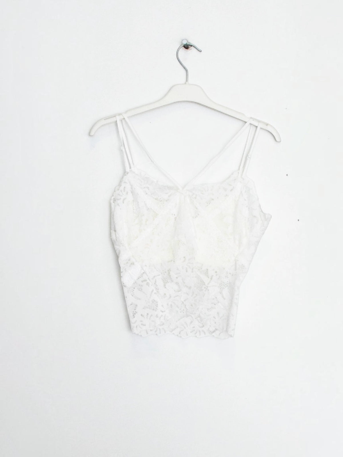 BROCK white lace crop top tank with built-in cups and delicate spaghetti straps hanging on a white hanger