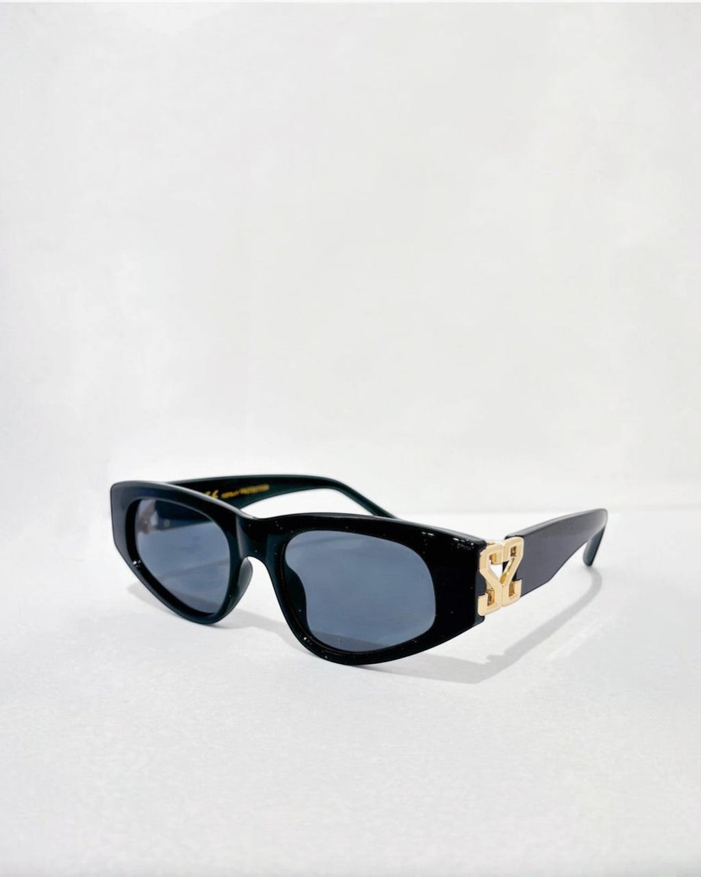 Lunettes de soleil ÉLINE L'ATELIER noires avec logo doré sur les branches, verres gris.