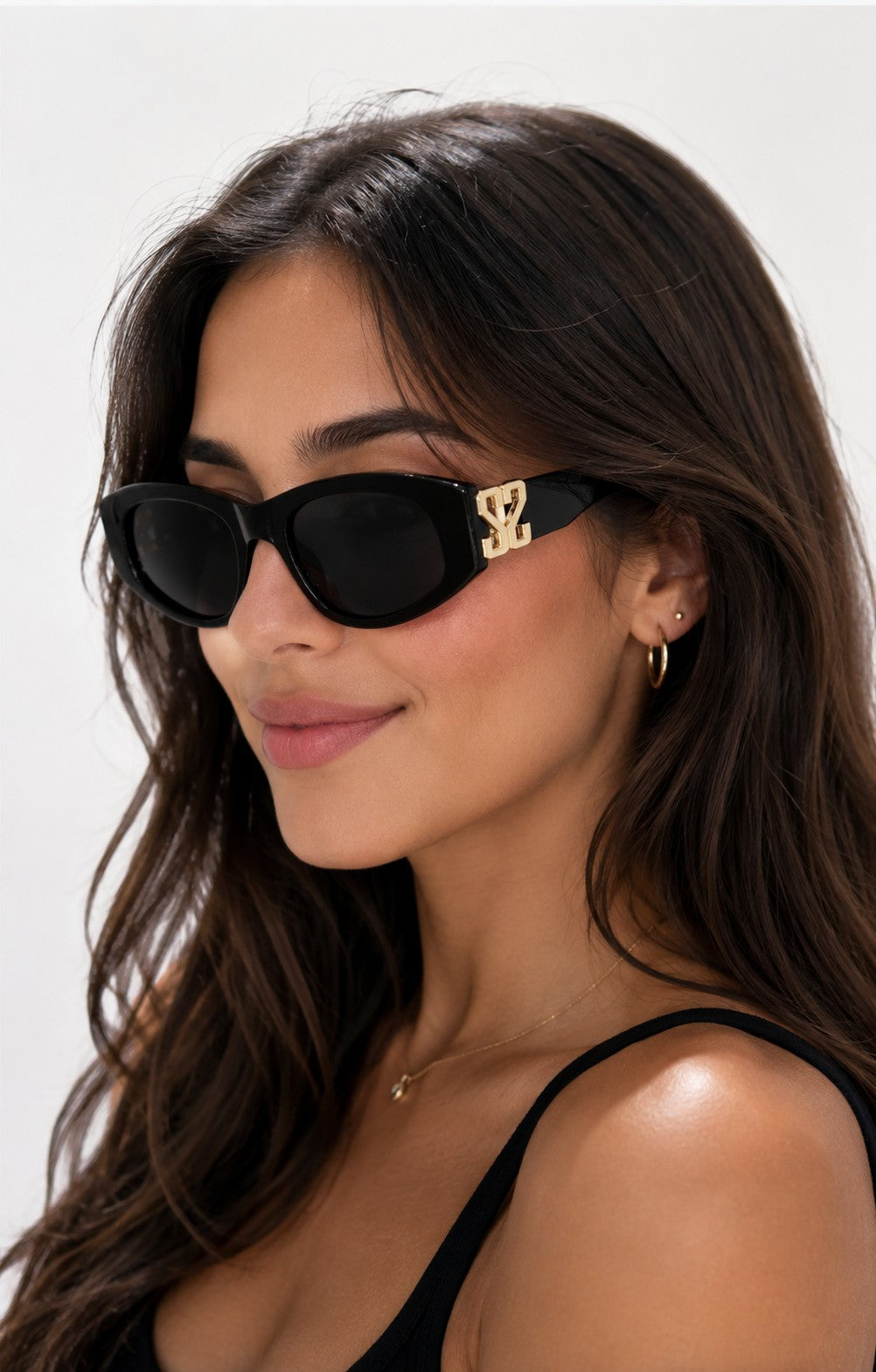 Lunettes de soleil ÉLINE L'ATELIER noires avec détails dorés sur les branches, monture épaisse et verres teintés.