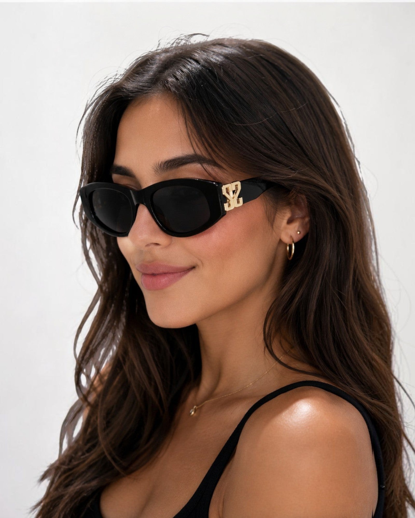 Lunettes de soleil ÉLINE L'ATELIER noires avec détails dorés sur les branches, monture épaisse et verres teintés.