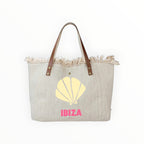 Grand sac cabas de plage  en toile beige avec anses en cuir, bords effilochés et motif coquillage Ibiza rose.