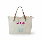 Grand sac cabas de plage  en toile beige avec anses en cuir, bords effilochés et inscription Miami Beach.