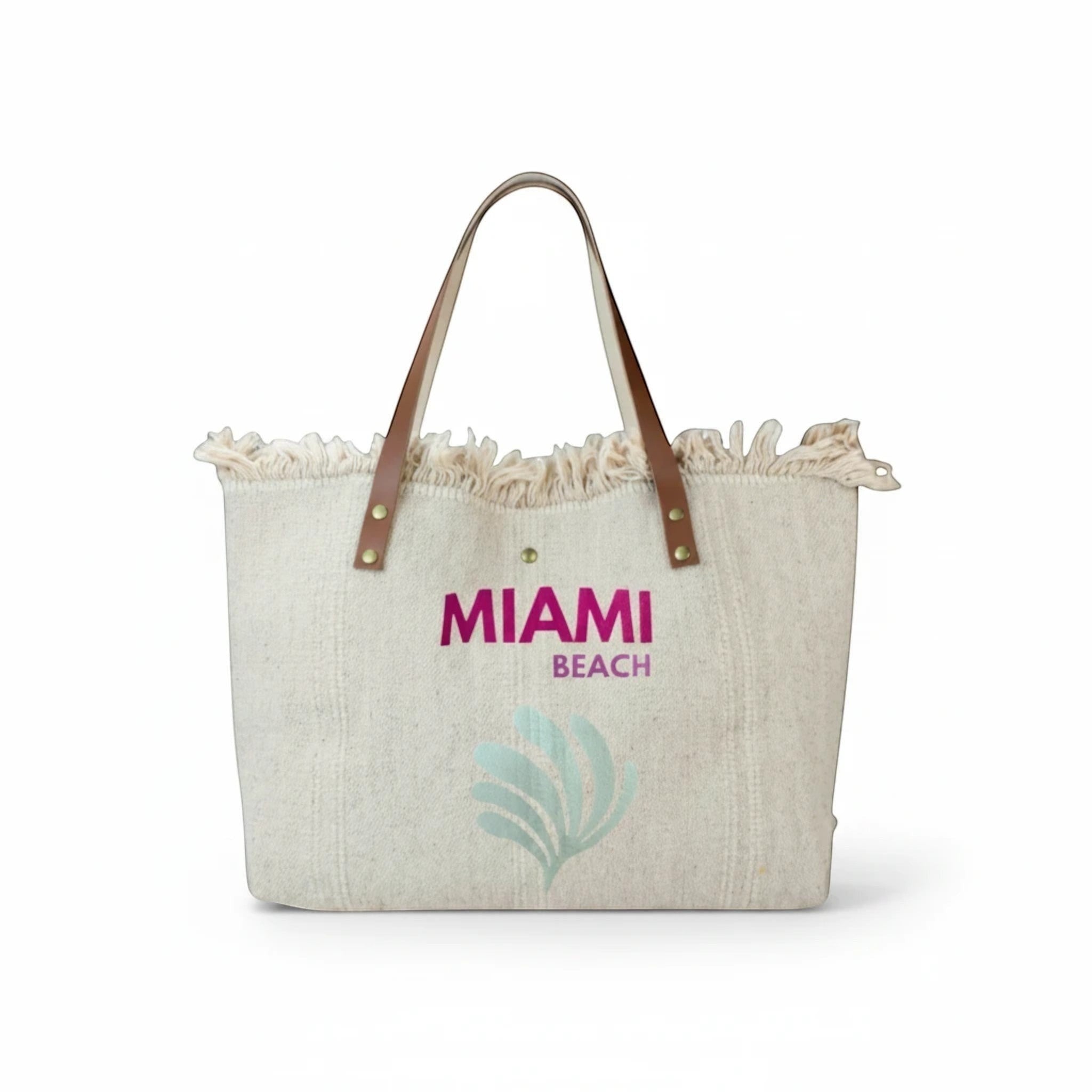 Grand sac cabas de plage  en toile beige avec anses en cuir, bords effilochés et inscription Miami Beach.