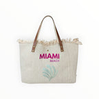 Grand sac cabas de plage  en toile beige avec anses en cuir, motif Miami Beach et bords effilochés bohèmes.