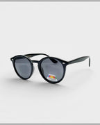 Lunettes de soleil ÉLINE L'ATELIER noires, monture ronde en plastique, verres polarisés et protection UV.