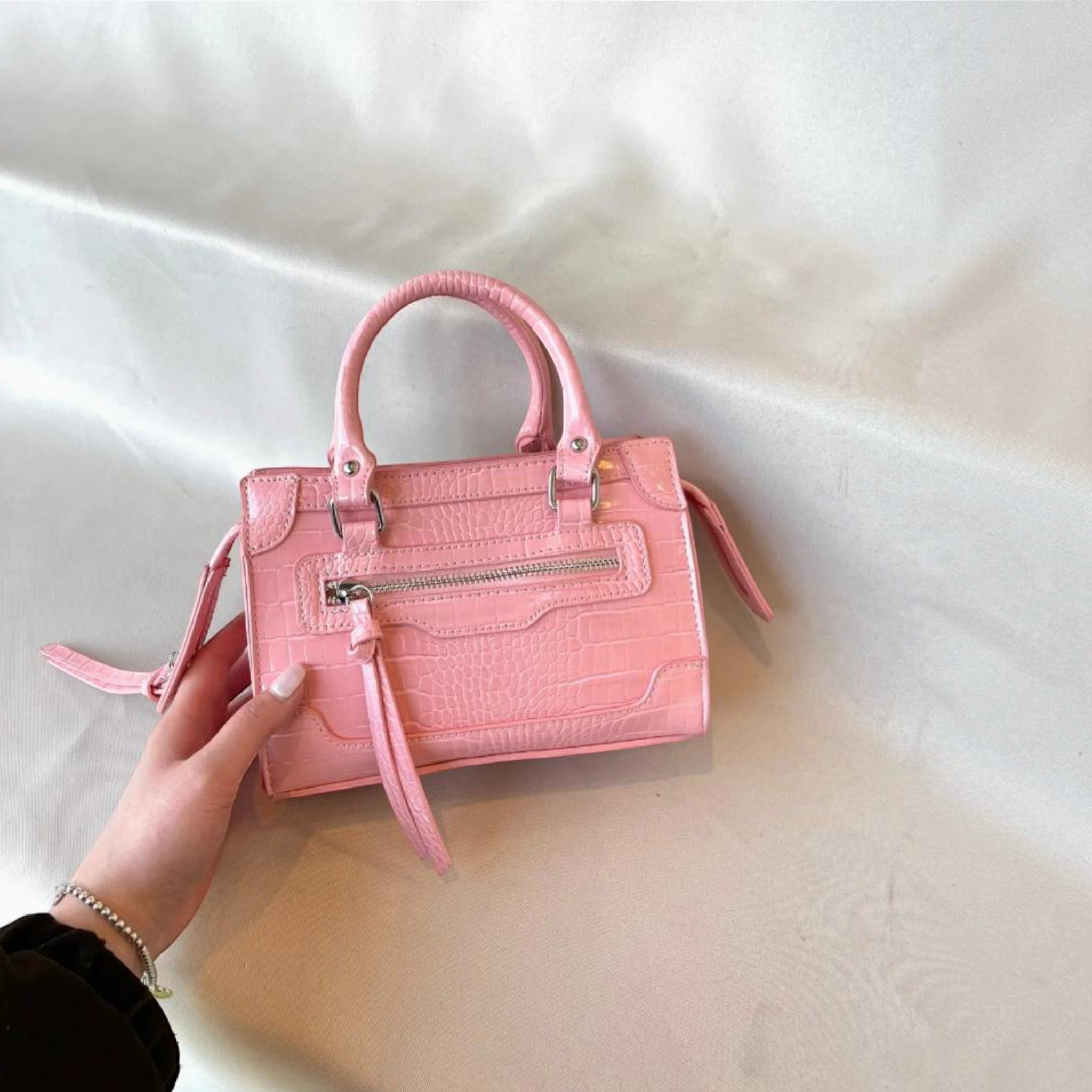 Sac à main structuré rose effet croco avec poignées et détails métalliques argentés, porté à la main.