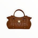 Sac à main LOUISA LEE en cuir grainé marron avec fermoir cadenas doré et clous dorés. Porté main ou épaule.
